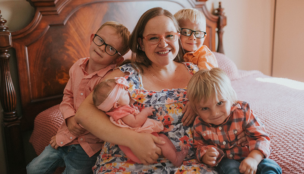 Carriann and her four children smiling together on a bed.