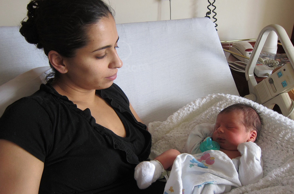Adriana in black blouse, gazing at her sleeping infant.