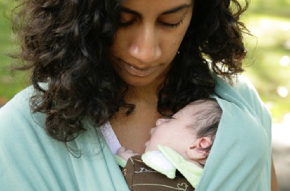 Divya gazes at her infant in a blue carrier.