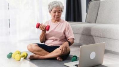Asian elderly woman learning to lift dumbbells from a video guide on a laptop.