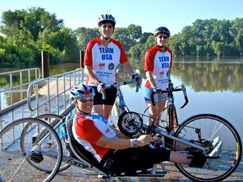 El equipo de EE. UU., con Shellie Pfohl, Karlin Hayes (de pie, de izquierda a derecha) y Susan Katz (sentada), a orillas del río Misuri en julio del 2010, en la línea de salida de RAGBRAI, una travesía en bicicleta de una semana a lo largo del estado de Iowa.