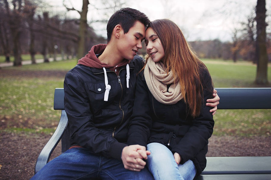 Teen couple holding hands on a park bench